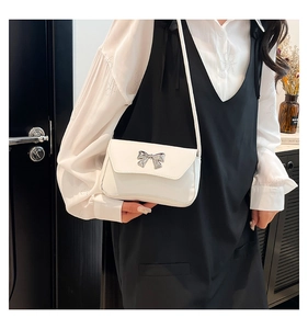 Close-up of a white square flap bag featuring a delicate silver metal bow buckle detail