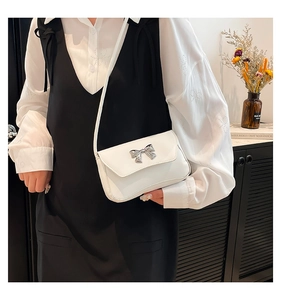 Detail shot of white rectangle flap bag with silver metal bow and leather strap