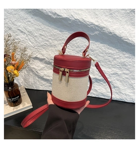 Detail view of a beige canvas bucket bag with dark red leather trim and gold hardware