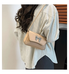 Beige small square bag with silver metal bow detail shown on shoulder with PU leather strap