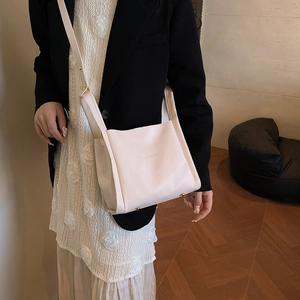 Minimalist beige pebble leather bucket bag with wide strap and gold metal rivets
