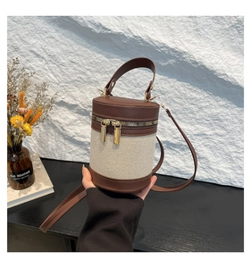 Detail of a brown and beige canvas bucket bag with dual zippers and gold hardware