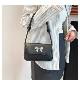 Detail of black faux leather shoulder bag with a silver butterfly buckle and knotted strap