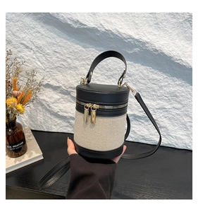 Detail of beige canvas and black leather bucket bag with gold zipper and handle