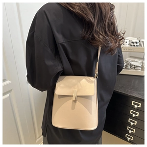 Gros plan du sac bandoulière beige avec boucle dorée sur une chemise noire élégante