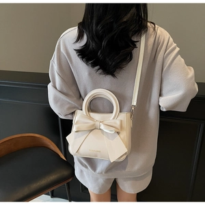 Detail of creamy white square bag featuring a large bow and metallic ring handle