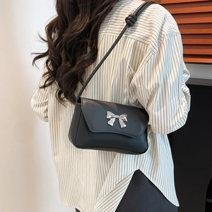 Minimalist black square shoulder bag with silver bow buckle worn by a model in casual style