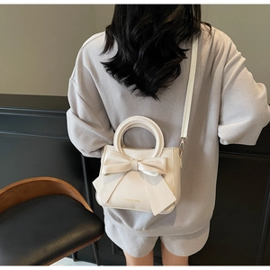 Close-up of cream square bag featuring a large decorative bow and golden fashion lettering