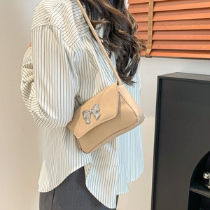 Beige rectangular crossbody bag with silver bow accent worn by a model in casual style