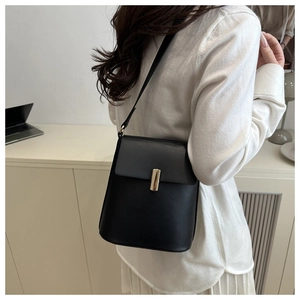 Sac bandoulière minimaliste en cuir noir avec fermoir doré porté par un mannequin