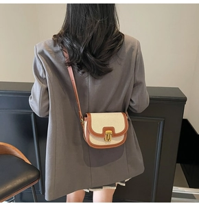 Detail view of canvas saddle bag with brown leather trim worn with a grey blazer