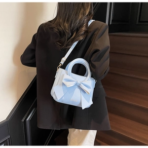 Close-up of light blue crossbody bag featuring a large decorative bow on the front