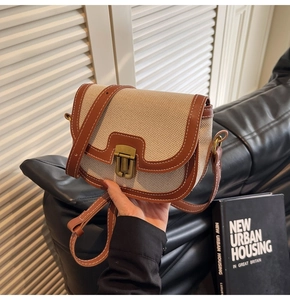 Detail of white canvas saddle bag with brown leather trim and brass buckle closure