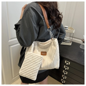 Detail of cream corduroy tote bag featuring a leather logo patch and silver chain strap