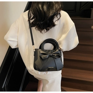 Detail of a black bow handbag with FASHION & BAGS lettering shown on a model