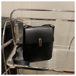 Détail d'un sac bandoulière noir avec une boucle cylindrique dorée et un rabat chic