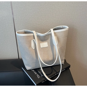 Close-up of beige canvas tote bag with white leather straps resting on a book