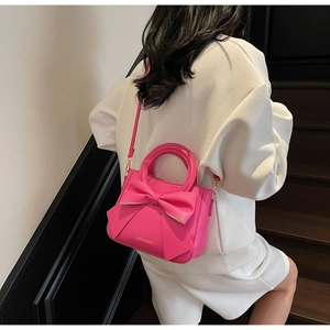 Lifestyle shot of fuchsia square crossbody bag with oversized bow and metal hooks