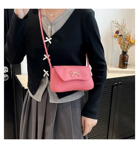 Detail of pink crossbody bag with elegant golden metal bow and leather texture