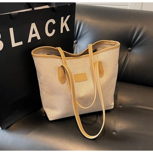 Detail of beige canvas tote bag with light brown leather trim on a black leather sofa