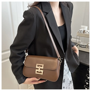 Brown leather crossbody bag with gold buckle detail shown on a model in a blazer
