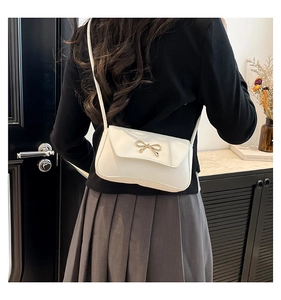 Close-up of white leather square bag with gold bow clasp worn as a shoulder bag
