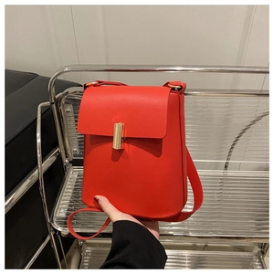 Gros plan d'un sac bandoulière rouge avec fermoir rotatif doré et texture en similicuir