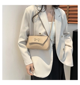 Detail of elegant beige shoulder bag with a gold metal bow clasp on minimalist flap
