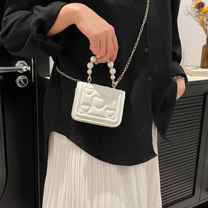 White mini square shoulder bag with heart embossing and pearl handle held by a model