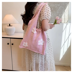 Detailed close-up of a pink knitted tote bag with white flower patterns on a model