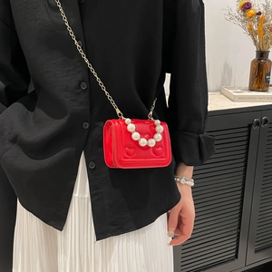 Red quilted heart handbag with pearl handle and gold chain strap worn by a model