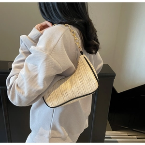 Detailed close-up of cream woven underarm bag with black trim and golden chain strap
