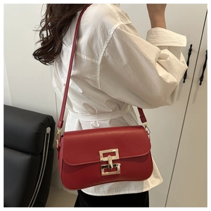 Detail view of red matte leather crossbody bag with a gold buckle worn by a model