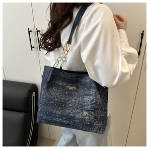 Detail of blue denim tote bag with rhinestones and gold chain strap on shoulder