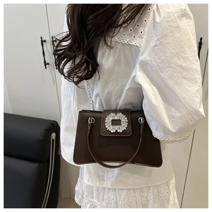Vue détaillée d'un sac à main marron chic avec boucle en strass porté sur une robe blanche