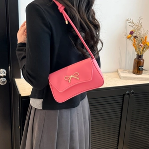Pink leather crossbody bag with gold bow clasp worn by a model in a trendy casual style