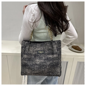 Detail of grey tweed tote bag featuring gold chain strap and vintage leather logo tag