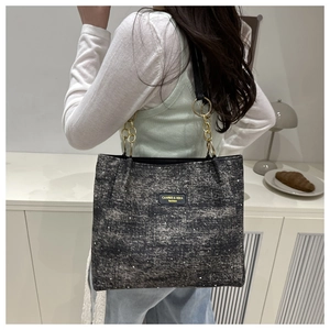 Detail of dark grey tweed tote bag with sequins and elegant chain strap on a model