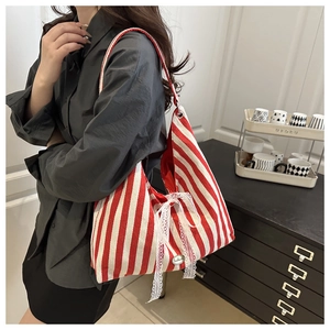 Detail of red and white striped tote bag with lace bow and metal logo on a shoulder strap