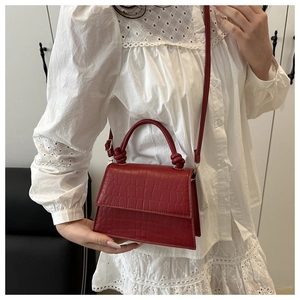 Detail of red crocodile textured leather bag with unique knotted handle on lace top
