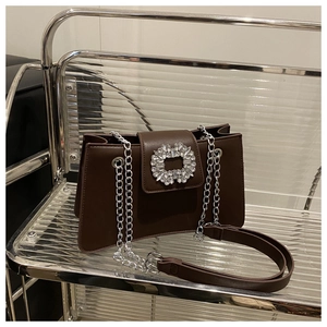 Détail du sac bandoulière marron chocolat avec une boucle en cristal et chaîne argentée
