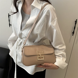 Minimalist beige crossbody bag with gold metal clasp and adjustable strap on a white shirt