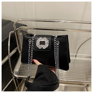 Détail d'un sac en cuir noir avec boucle carrée en cristal et bandoulière en chaîne argentée