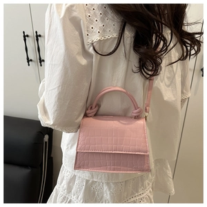Pink croc-embossed mini crossbody bag with a knotted handle detail shown on a model