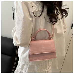 Detail of pink croc-embossed square bag with knot handle and detachable strap on model