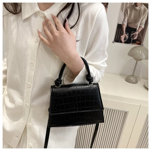 Detail of black crocodile texture mini bag with golden hardware and knot handle