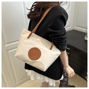 Detail of a beige nylon tote with brown leather handles and a circular fashion logo