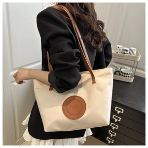 Detailed view of canvas tote bag with brown leather straps and fashion bags logo patch