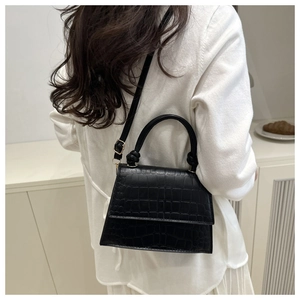 Detail view of black crocodile pattern crossbody bag on model in a soft lit setting