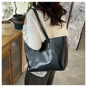Close-up of black glossy tote bag showing textured pleats and shoulder strap detail